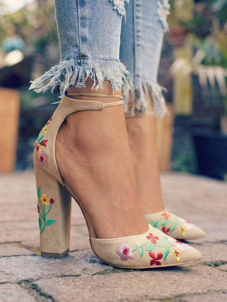 Chaussures beiges à talons hauts ornées de broderies florales, portées avec un jean déchiré sur un fond extérieur flou.