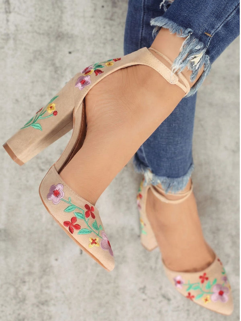 Beige high-heeled shoes with floral embroidery worn with ripped jeans on a neutral background