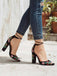 Black block-heeled shoes with floral embroidery worn with blue jeans on a light background.