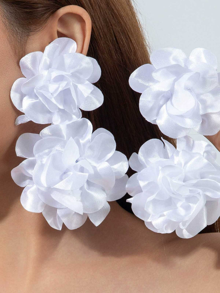 Modèle présentant de grandes boucles d'oreilles en tissu blanc ornées de fleurs, idéales pour une mariée ou une tenue élégante pour une occasion estivale.