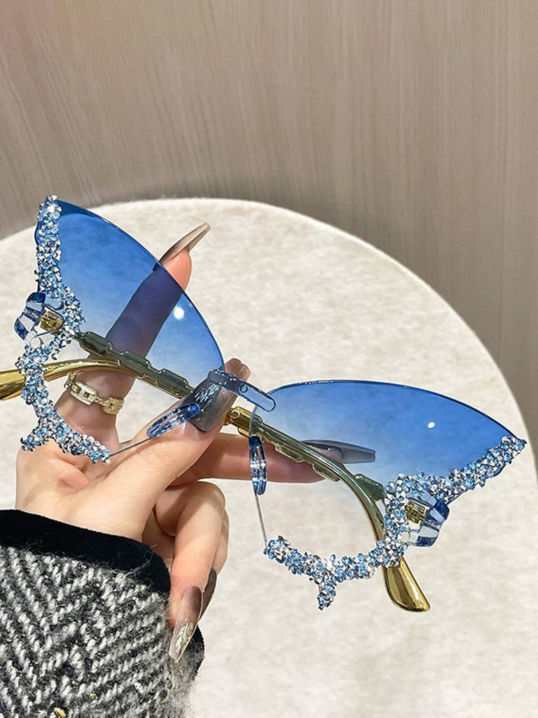 Blue butterfly-shaped sunglasses with gold accents held by a hand against a neutral background