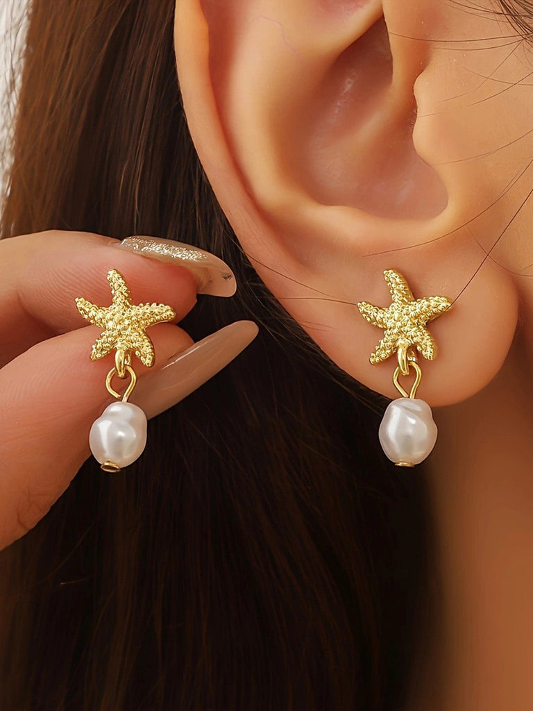 Boucles d'oreilles en forme d'étoile de mer dorée avec des gouttes de perles, portées par une personne.