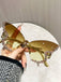 Gold sunglasses with decorative elements held by a hand against a neutral background