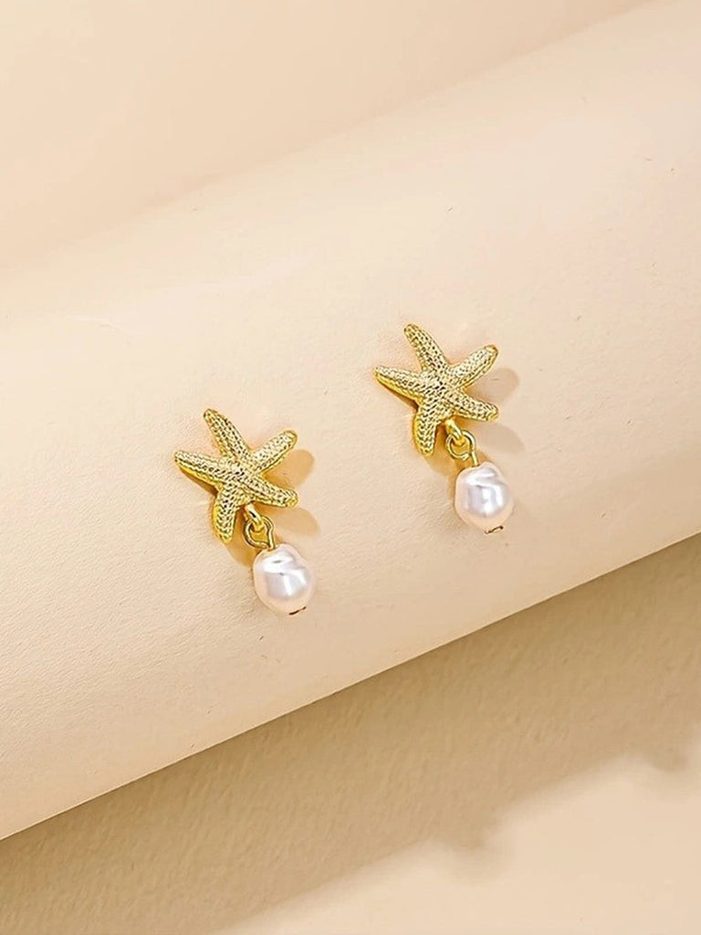 Gold starfish earrings with pearl drops on a beige background