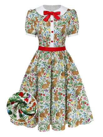 Une robe trapèze à manches courtes d'inspiration vintage, ornée d'un imprimé fantaisiste de lapins et de fleurs sauvages, d'un col Claudine blanc et d'un nœud rouge décoratif.
