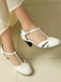 White medium-heeled shoes worn by a person on a light wooden floor.