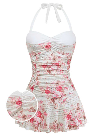 A white one-piece swimsuit featuring a pink rose print, vintage cursive script, a sweetheart neckline, and an attached ruffled swim skirt.
